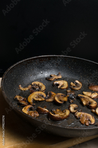 Fried mushrooms in frying pan on wooden table. Dish for dinner. Close up view