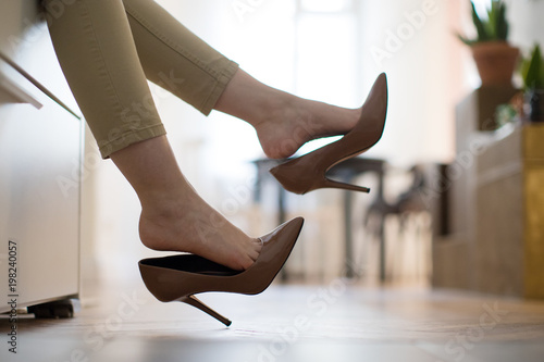 Tired woman is resting taking off her brown high-heeled shoes after work or walking, lying on the sofa. uncomfortable shoes