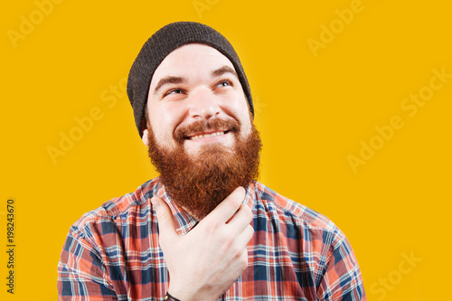 Emotions concept. Surprised handsome hipster man touching his beard while posing in studio. Barbershop concept. Bearded hipster man thinking and smiling.