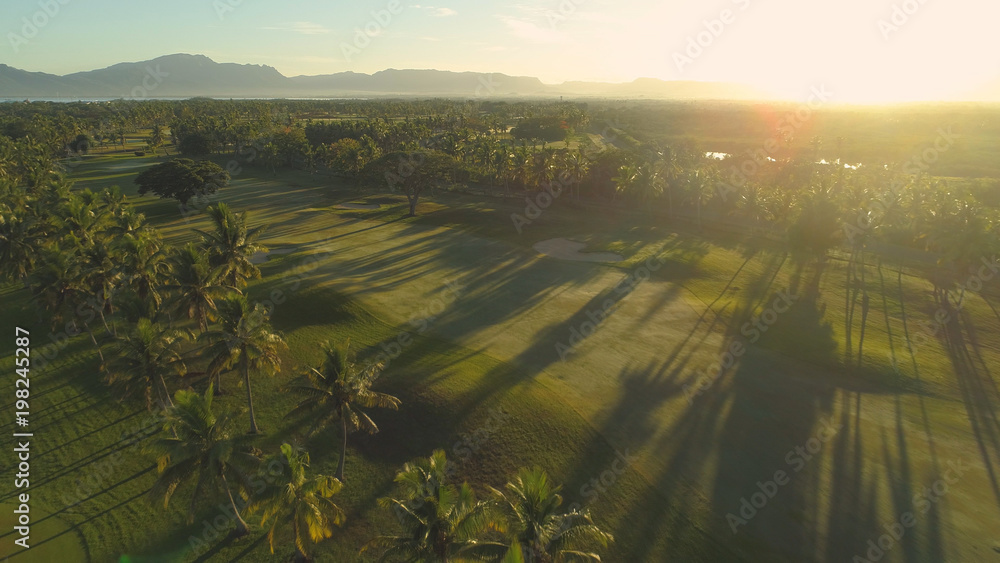 AERIAL: Cinematic view of empty golden-lit golf course on the exotic island.