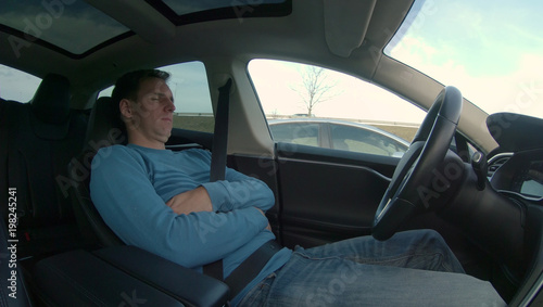 Man relaxes while his high tech self driving car navigates through rush hour