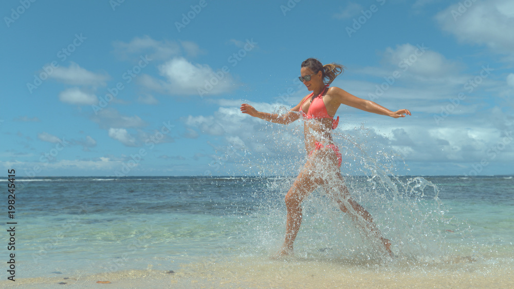 Smiling woman plays by the beach and splashes crystal clear sea water everywhere