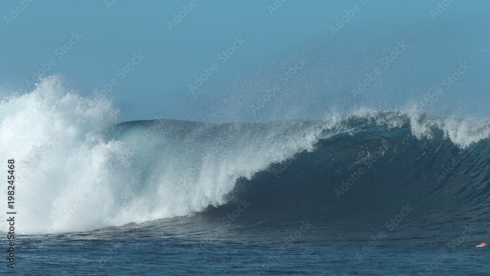 Big blue barrel wave crashes forcefully and splashes fresh sea water everywhere.