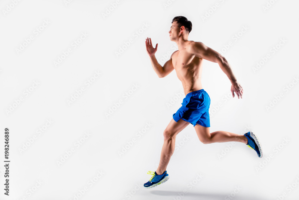 Ready, steady, go! Handsome muscular strong determined guy dressed in blue shorts and sneakers is running to the finish line, isolated on white background, copy-space