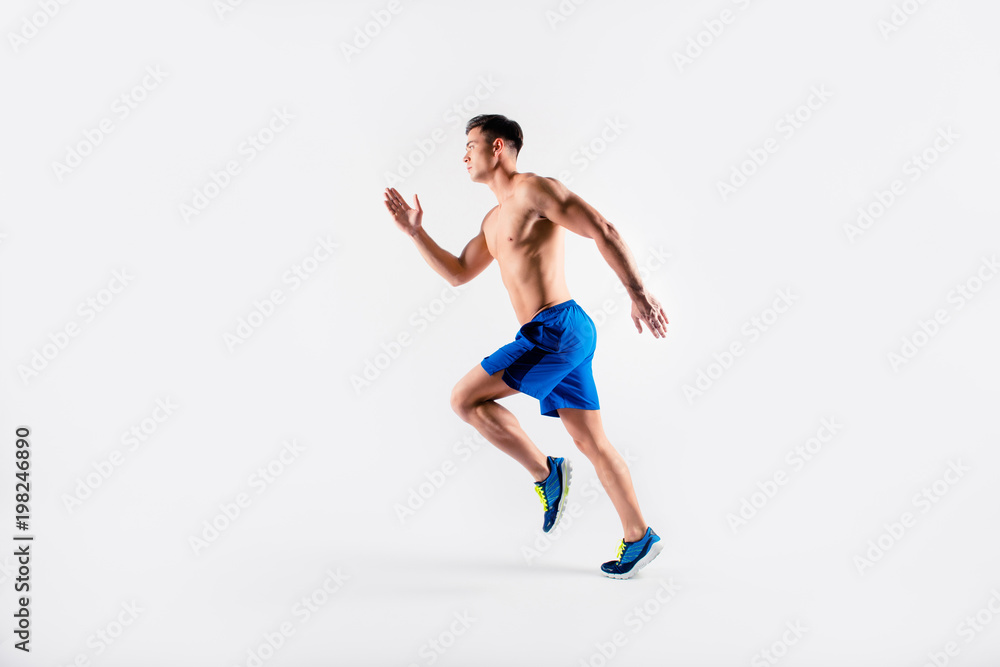 Portrait of concentrated confident muscular full of strength sportsman wearing shorts and sneakers, he is running a marathon, isolated on white background