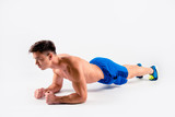 Side profile view photo of handsome active confident serious muscular young athlete wearing blue shorts and sneakers, he is doing plank on the floor, isolated on white background