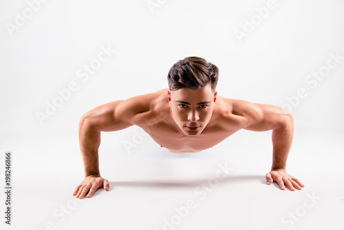 Close up photo of a sportive muscular handsome diligent determined athlete doing push ups from the floor, isolated on white background