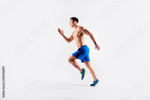 Portrait of concentrated confident muscular full of strength sportsman wearing shorts and sneakers, he is running a marathon, isolated on white background