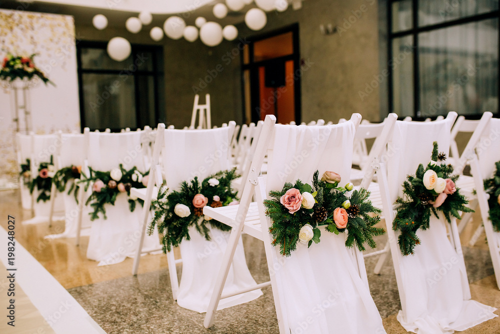 close-up of white chairs decorated with flowers, spruce and cloth on a wedding arch background