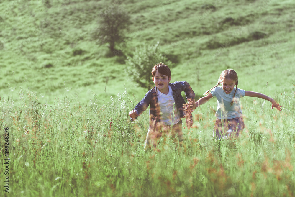 Joyful children are running on meadow. They are holding hands and laughing with excitement. Copy space Joyful children are running on meadow. They are holding hands and laughing with excitement. Copy space