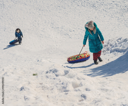 children climbing the hill and pulling inflatable snow tube