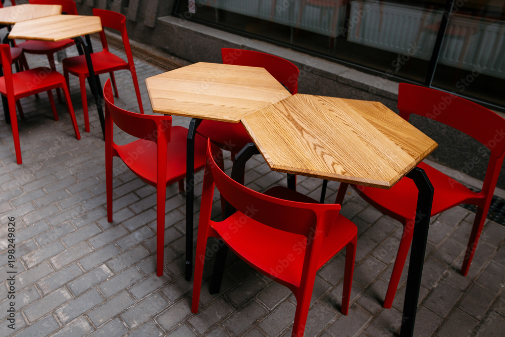 stylish wooden tables and red steel chairs in city street. stylish modern settings, cafe terrace outdoors