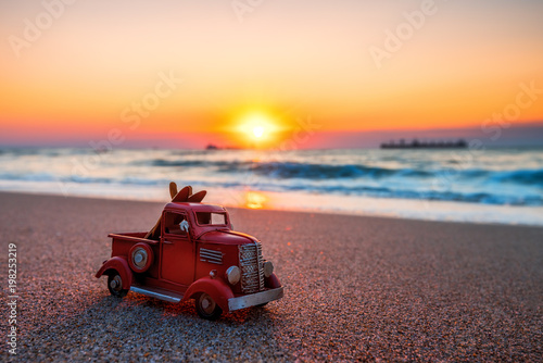 Sunrise on tropical island beach and car truck miniature. Travel concept.