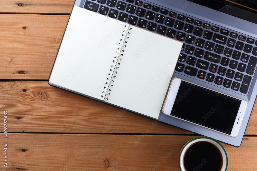Laptop and cup of coffee on a wooden background, workstation on an old desk, smartphone and a notebook, pen and glasses in the workplace, designer workstation, art Laptop and cup of coffee on a wooden background, workstation on an old desk, smartphone and a notebook, pen and glasses in the workplace, designer workstation, art