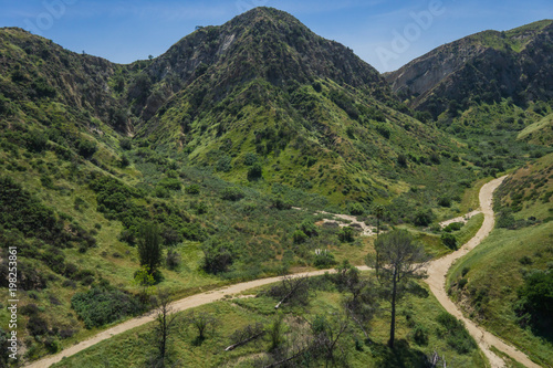 Dirt walking trails come together beneath grass covered California hills.