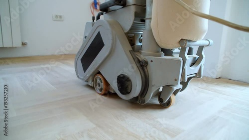 Sanding hardwood floor with the grinding machine. Repair in the apartment. Carpenter doing parquet wood floor polishing maintenance work by grinding machine