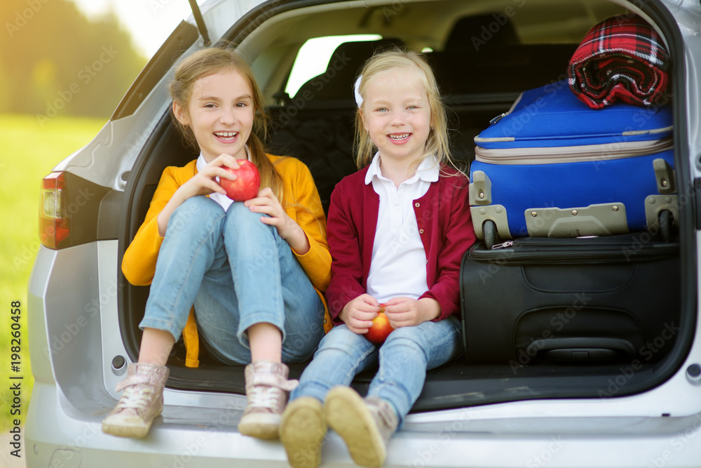 Two adorable little girls sitting in a car before going on vacations with their parents. Two kids looking forward for a road trip or travel.