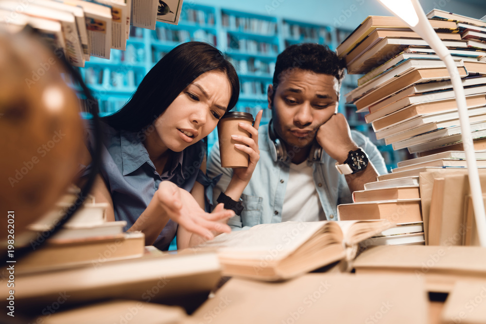 Ethnic asian girl and indian mixed race guy surrounded by books in library. Students are reading book. Ethnic asian girl and indian mixed race guy surrounded by books in library. Students are reading book.