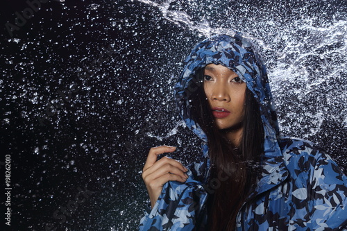 Active Woman rain coat with Water Splash over studio lighting black backgrounds