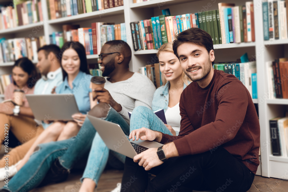 Group of ethnic multicultural students sitting near bookshelf in library. Group of ethnic multicultural students sitting near bookshelf in library.
