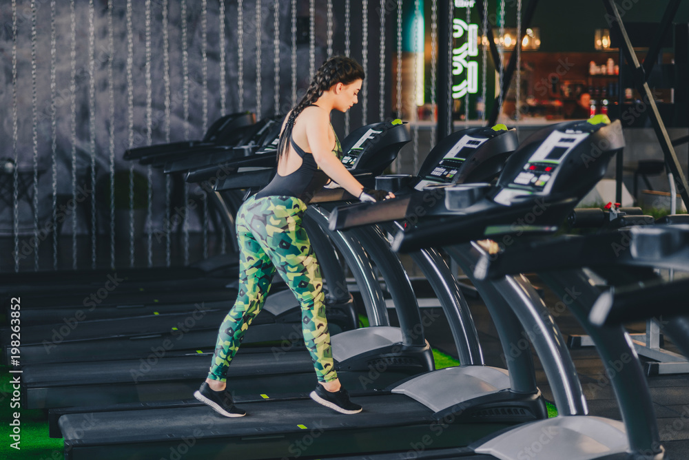 Obraz premium Attractive young fitness model runs on a treadmill, is engaged in fitness sport club