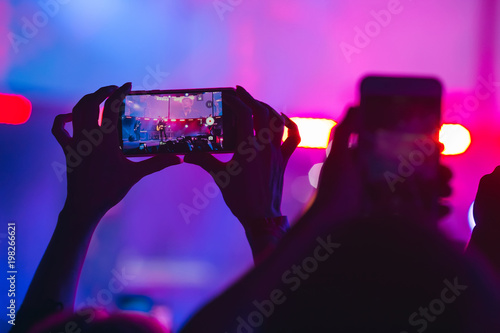 People hands with smartphone. Recording video or shooting photo at music festival, rock concert. blue magenta background