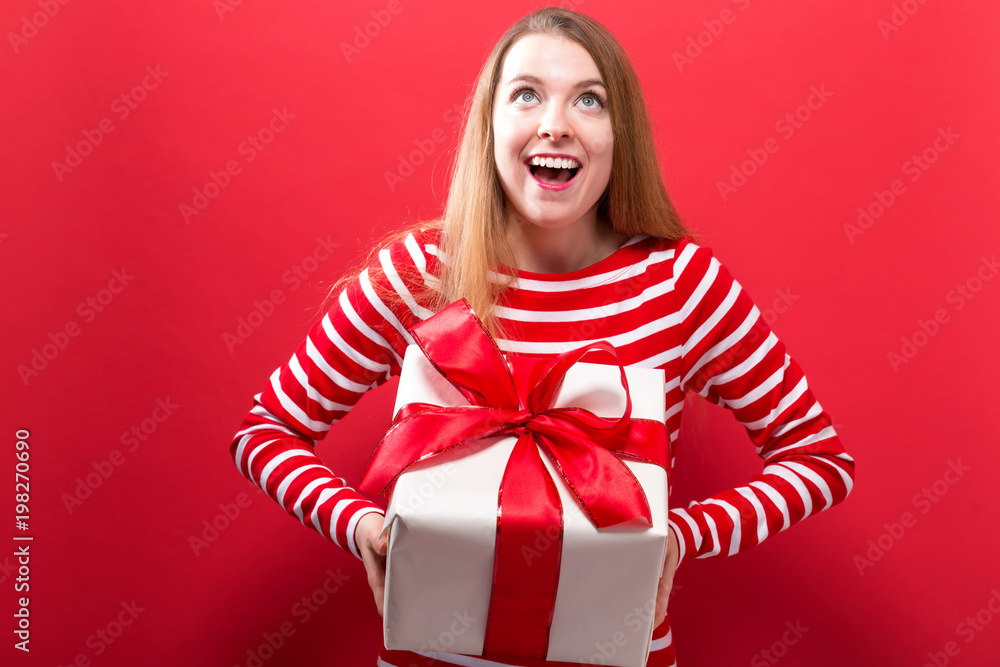 Happy young woman holding a gift box on a red background Happy young woman holding a gift box on a red background