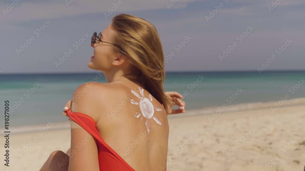 Happy couple applying sun tanning lotion on the beach, man putting sunscreen suntan cream on woman - video in slow motion Happy couple applying sun tanning lotion on the beach, man putting sunscreen suntan cream on woman - video in slow motion
