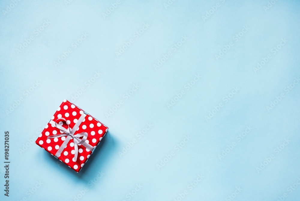 Top view of a red dotted gift box tied with silver bow over blue background. Copy space. Top view of a red dotted gift box tied with silver bow over blue background. Copy space.