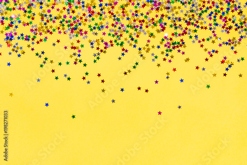 Scattered star shaped colorful glittering confetti over yellow background. Copy space.