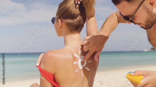 Happy couple applying sun tanning lotion on the beach, man putting sunscreen suntan cream on woman