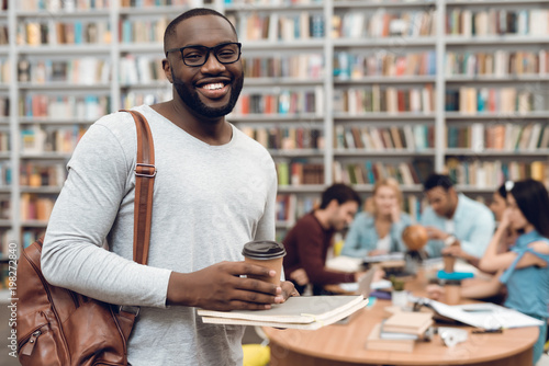 Group of ethnic multicultural students in library. Black guy with notes and coffee.