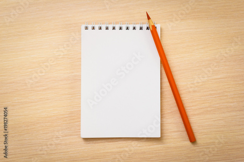 Orange pencil with notebook on wooden table © morkovkapiy