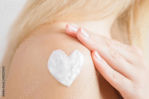 Groomed woman's hand applying moisturizing cream on her shoulder. Cares about clean and soft body skin. Heart shape created from cream. Love a body. Healthcare concept. photo