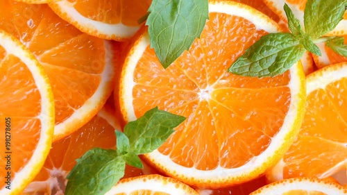 Slow pan of fresh bright oranges (orange fruits) slices decorated with mint leaves. Closeup.