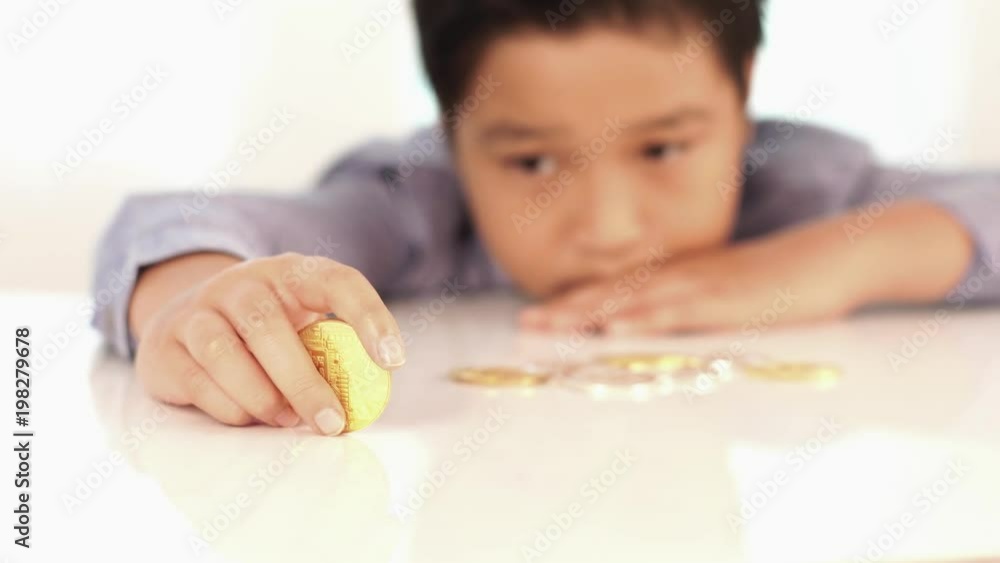 4k young Asian Thai boy looking at golden Bitcoin , a digital symbol of virtual currency in his finger play on white table. 4k young Asian Thai boy looking at golden Bitcoin , a digital symbol of virtual currency in his finger play on white table.
