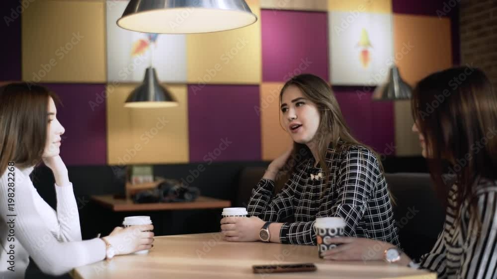 Friends in a cafe bar. Girls drink coffee in a cafe. Three girlfriends are sitting at a table in a cafe.