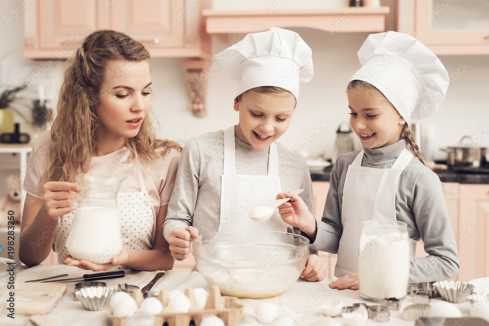 Children with mother in kitchen. Kids are adding flour and mother is adding milk in bowl. Children with mother in kitchen. Kids are adding flour and mother is adding milk in bowl.