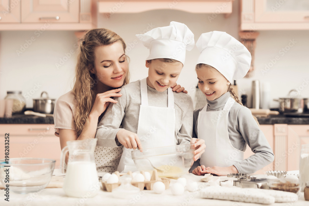 Children with mother in kitchen. Brother is whisking eggs with fork.