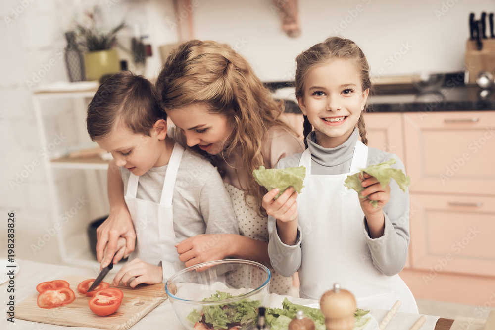 Children with mother in kitchen. Mother is helping kids prepare vegetables for salad.
