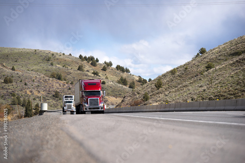 Modern big rigs convoy moving on the road between the hills in Idaho