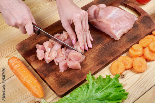Female hands with a knife, cuts the meat on the wooden board . Healthy eating and lifestyle.