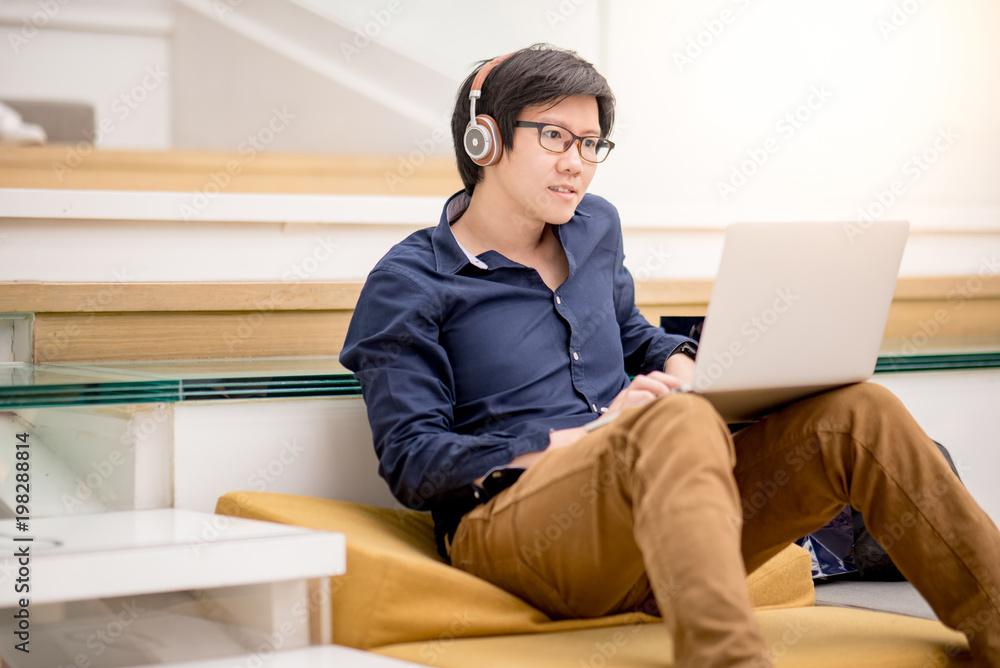 Young Asian business man enjoy watching movie online with laptop computer on ths stair in living space. relaxing urban lifestyle in accommodation concepts Young Asian business man enjoy watching movie online with laptop computer on ths stair in living space. relaxing urban lifestyle in accommodation concepts