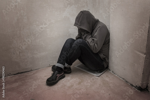 Canvas Print Photo of desperate young drug addict wearing hood and sitting alone in corner