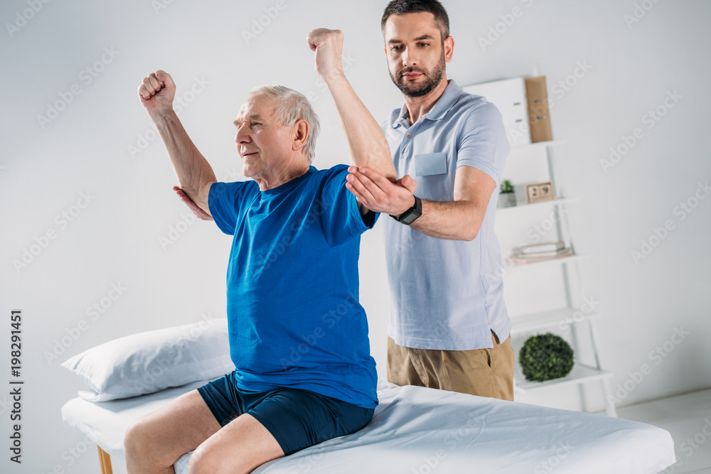 Obraz premium portrait of focused physiotherapist doing massage to senior man on massage table