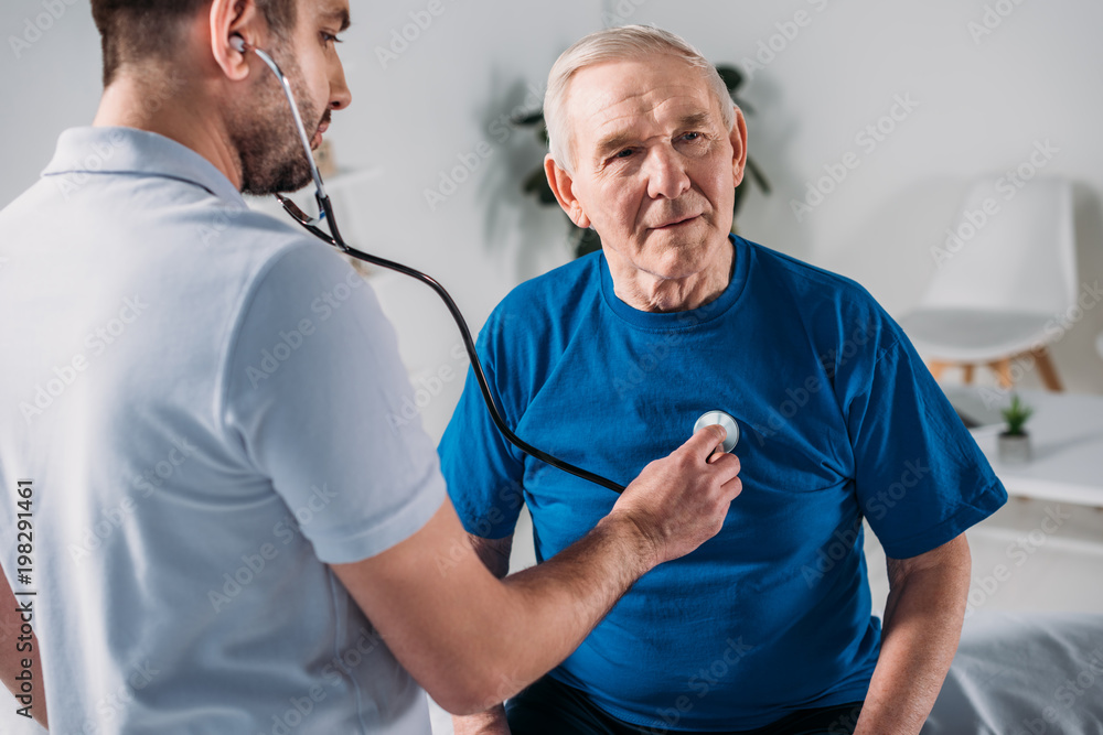 rehabilitation therapist with stethoscope checking senior mans heartbeat rehabilitation therapist with stethoscope checking senior mans heartbeat