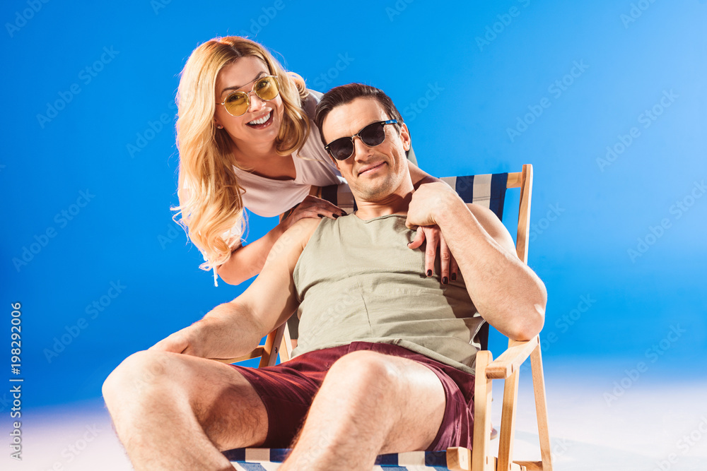 Woman hugging man relaxing in deck chair on blue background