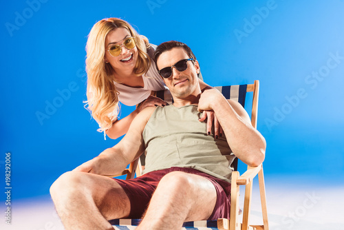 Woman hugging man relaxing in deck chair on blue background
