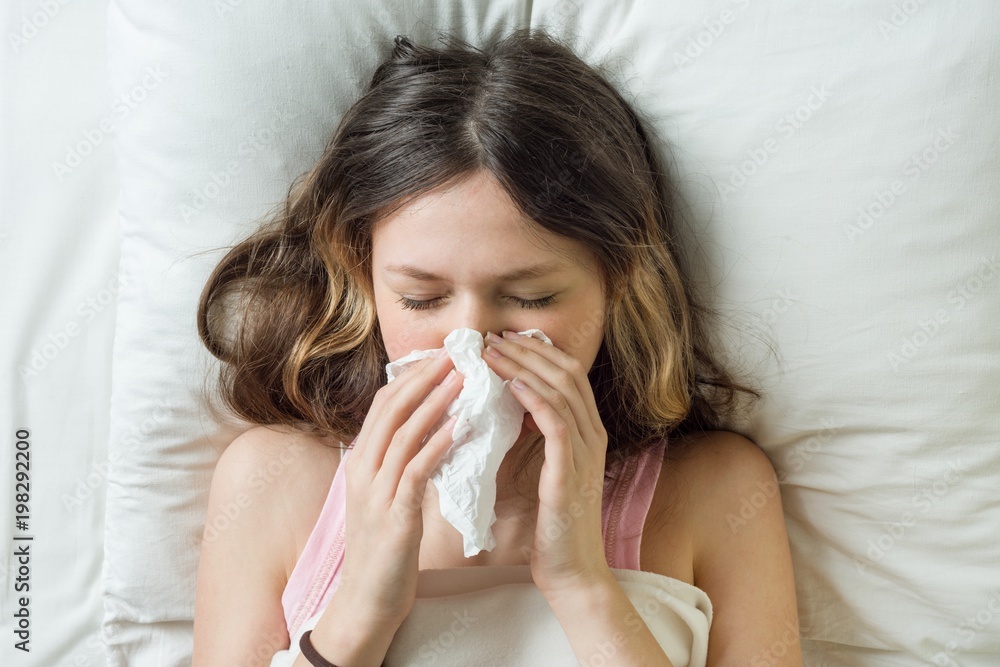 Cold flu season, runny nose. Sick girl on bed sneezing in handkerchief in bedroom Cold flu season, runny nose. Sick girl on bed sneezing in handkerchief in bedroom