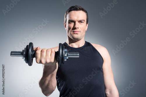 Young man athlete exercising with dumbbell on grey background